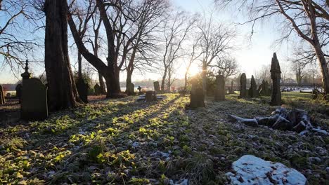 Flying-FPV-around-headstones-in-snowy-autumn-sunrise-churchyard-cemetery-during-golden-hour