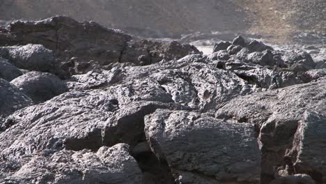 detail-of-solidified-lava-with-some-steam-rising,-slope-of-a-hill-in-background
