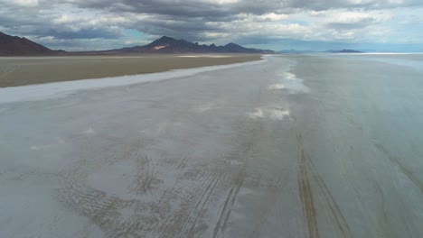 Aerial-view-of-big-salt-flats-with-the-sky-mirroring-in-them-and-mountains-and-clouds-in-the-background