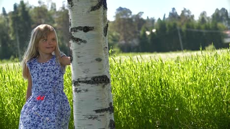 Static-portrait,-Young-girl-in-summer-dress-standing-next-to-birch-tree,-idyllic-summer-meadow,-looking-into-camera