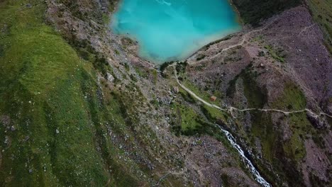 Aerial,-tilt,-drone-shot-overlooking-crystal-clear,-blue-water-of-lake-Humantay,-in-the-Andes-mountains,-on-a-cloudy-day,-in-Peru,-South-America