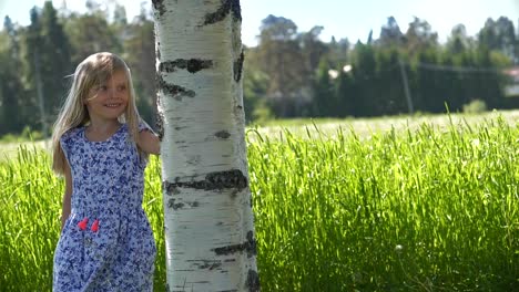 Smiling-little-blond-girl-near-birch-tree-on-summer-day