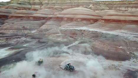 Aerial-View-of-Man-Spinning-With-ATV-Quad-in-Dusty-Canyon-Under-Striped-Sandstone-Hills-in-Utah-Desert,-USA
