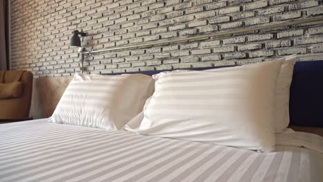 Panning-shot-of-white-pillows-and-linen-sheets-on-hotel-room-bed