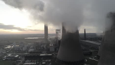 Aerial-shot-of-atmospheric-power-station-cooling-towers-smoke-steam-emissions-overlooking-sunrise-horizon