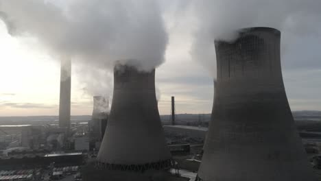 Aerial-view-rising-to-UK-power-station-cooling-towers-atmospheric-smoke-steam-emissions-at-sunrise