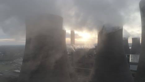 Aerial-slow-dolly-right-across-power-station-cooling-towers-smoke-steam-emissions-above-sunrise-glow