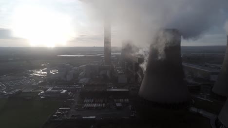 Aerial-lowering-pull-back-UK-power-station-cooling-towers-below-smoke-steam-emissions-at-sunrise