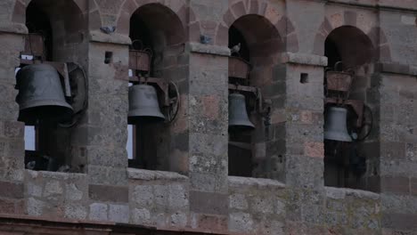 A-close-shot-of-four-bells-in-a-bell-tower,-with-some-pigeons-on-it