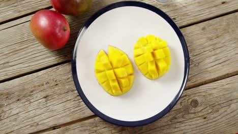 Halved-and-chopped-mango-with-glass-of-water-on-wooden-table
