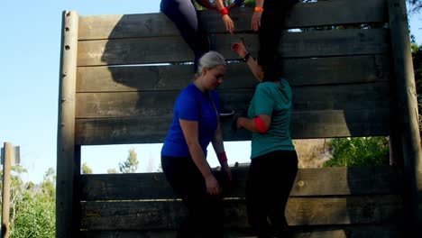 Woman-being-assisted-by-her-teammates-to-climb-a-wooden-wall-during-obstacle-course