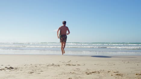 Man-running-with-surfboard-at-beach-on-a-sunny-day