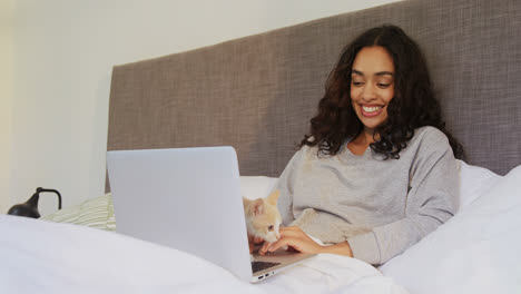 Happy-woman-using-her-laptop-while-sitting-on-bed-with-her-cat-4K-4k
