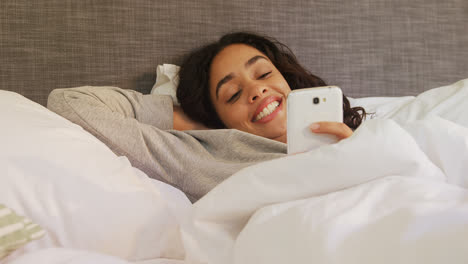 Happy-young-woman-lying-on-bed-using-her-mobile-phone-4K-4k