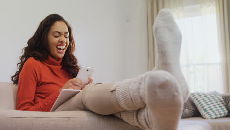 Woman-sitting-on-sofa-laughing-while-using-her-mobile-phone-4K-4k
