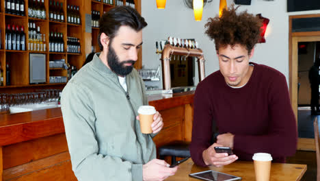Male-friends-using-mobile-phone-while-having-coffee-4k