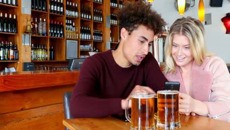 Couple-using-mobile-phone-while-having-glass-of-beer-4k