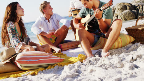 Man-playing-guitar-for-friends-sitting-on-the-beach-4k