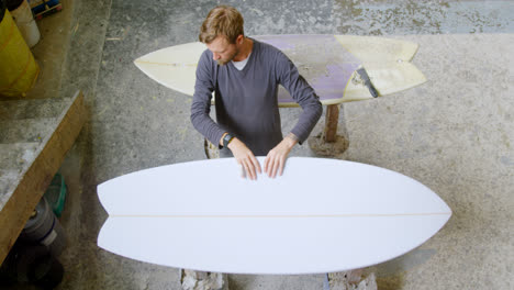Man-examining-a-surfboard-4k