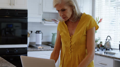 Senior-woman-using-laptop-in-kitchen-4k