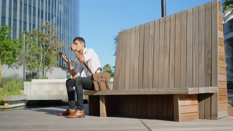 Man-talking-on-mobile-while-having-coffee-on-bench-4k