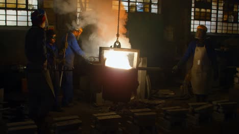 Gruppe-Von-Arbeitern,-Die-Einen-Behälter-Mit-Geschmolzenem-Metall-In-Der-Werkstatt-Tragen-4k