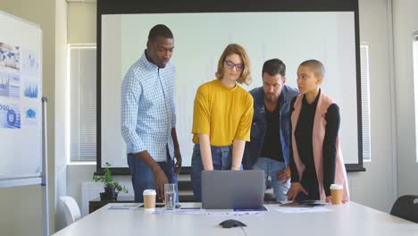 Front-view-of-mixed-race-business-team-discussing-over-laptop-in-modern-office-4k
