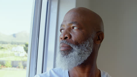Side-view-of-mature-black-man-looking-through-window-in-a-comfortable-home-4k