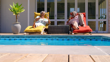 Vorderansicht-Eines-Schwarzen-Seniorenpaares,-Das-Sich-Auf-Dem-Liegestuhl-Am-Pool-Im-Hinterhof-Seines-Hauses-Entspannt,-4k