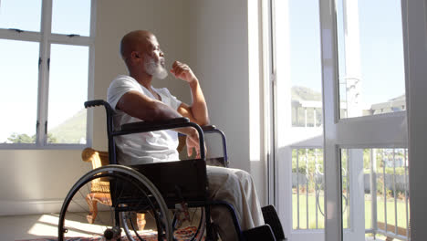 Side-view-of-mature-black-handicap-man-sitting-on-wheelchair-near-the-window-at-home-4k