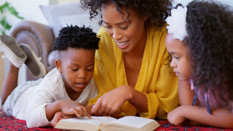 Vista-Frontal-De-Una-Madre-Negra-Con-Sus-Hijos-Leyendo-Un-Libro-En-Una-Casa-Cómoda-4k