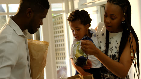 Front-view-of-young-black-mother-and-son-looking-in-grocery-bag-in-kitchen-of-comfortable-home-4k