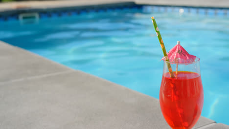 Close-up-of-cocktail-glass-with-umbrella-and-straw-near-swimming-pool-4k