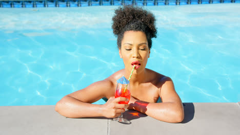 Front-view-of-young-mixed-racewoman-drinking-cocktail-in-swimming-pool-4k
