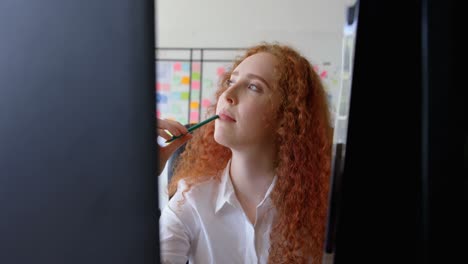 Front-view-of-thoughtful-young-caucasian-businesswoman-touching-her-lip-with-a-pencil-at-desk-4k