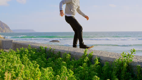 Seitenansicht-Eines-Jungen-Kaukasischen-Mannes,-Der-Auf-Dem-Bürgersteig-Am-Strand-Skateboard-Tricks-übt,-4k