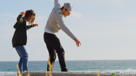 Side-view-of-young-caucasian-men-practicing-skateboard-trick-on-the-pavement-at-beach-4k