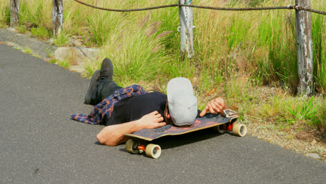 Modern-young-male-skateboarder-lying-on-the-road-with-his-head-on-a-skateboard-at-countryside-4k