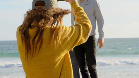 Rear-view-of-young-caucasian-woman-clicking-photo-of-young-caucasian-man-with-camera-on-the-beach-4k