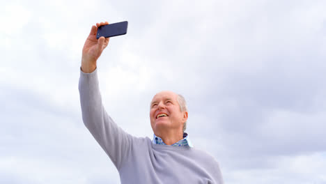 Vorderansicht-Eines-Alten-Kaukasischen-älteren-Mannes,-Der-Am-Strand-Ein-Selfie-Mit-Seinem-Mobiltelefon-Macht,-4k