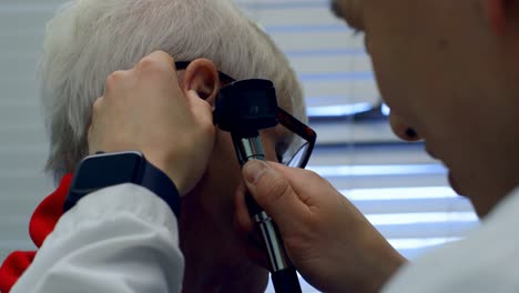 Young-Asian-male-doctor-examining-a-senior-patient-with-otoscope-in-the-clinic-4k