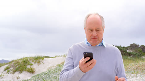 Front-view-of-old-caucasian-senior-man-using-mobile-phone-at-beach-4k