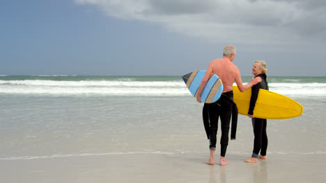 Old-caucasian-senior-couple-holding-surfboard-at-beach-4k
