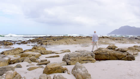 Rear-view-of-old-caucasian-senior-man-walking-over-rocks-at-beach-4k