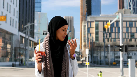 Vista-Frontal-De-Una-Joven-Asiática-Con-Hijab-Hablando-Por-Teléfono-Móvil-En-La-Ciudad-4k