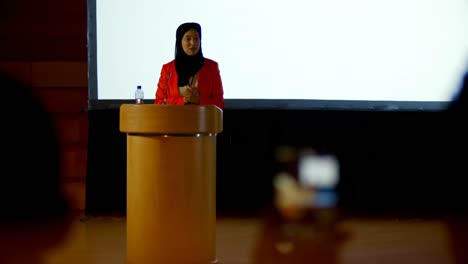 Mature-Caucasian-hijab-businesswoman-speaking-at-podium-in-auditorium-4k