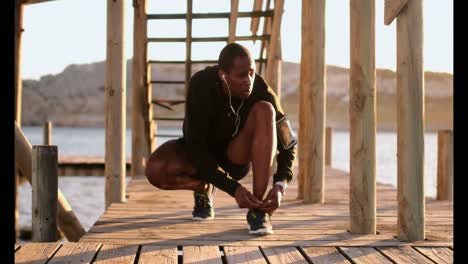 African-American-male-jogger-tying-shoelace-on-pier-at-beach-4k