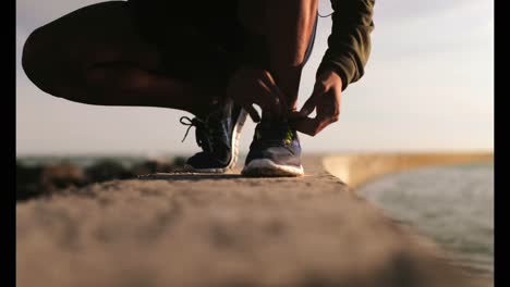African-American-male-jogger-tying-shoelace-on-the-beach-4k