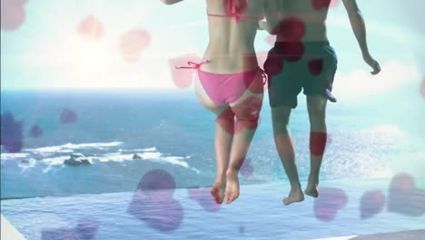 Couple-jumping-together-on-a-swimming-pool-with-the-ocean-on-the-background