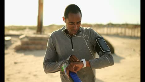 African-American-man-wearing-running-arm-band-and-using-smartwatch-at-beach-4k